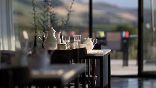 A table set with white teapots, cups, and glasses, with a view of hills through a glass door. - CASA PLENILIA (Pianella)