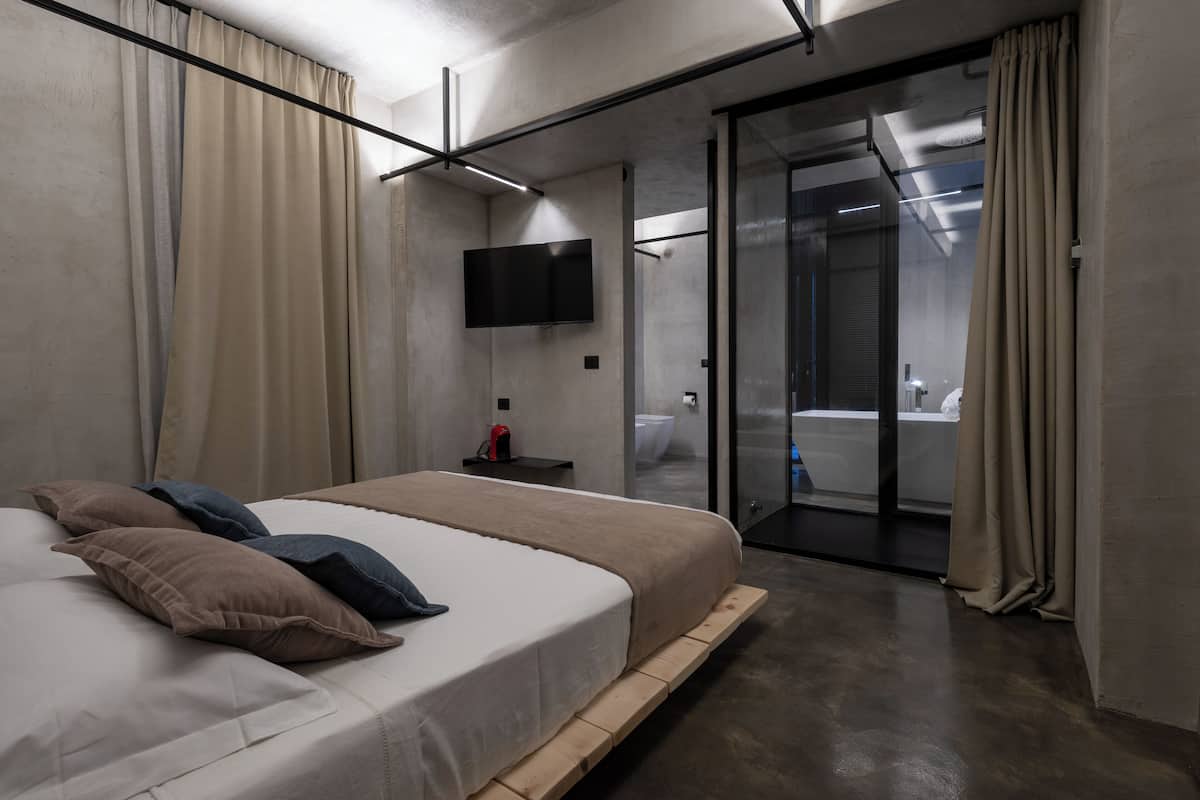 Habitación de hotel moderna con una cama grande, un televisor de pantalla plana, una puerta corredera de vidrio al baño y un diseño minimalista.