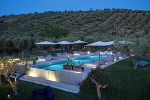 A modern outdoor pool area with multiple lounge chairs and umbrellas, surrounded by well-maintained grass and trees. - CASA PLENILIA (Pianella)