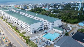 A large hotel with multiple floors, a swimming pool, and a view of the ocean. - Seas You Later - 2 Bedroom Condo Just 2 Blocks from the Beach with Large Pool, Elevator (Oak Island)