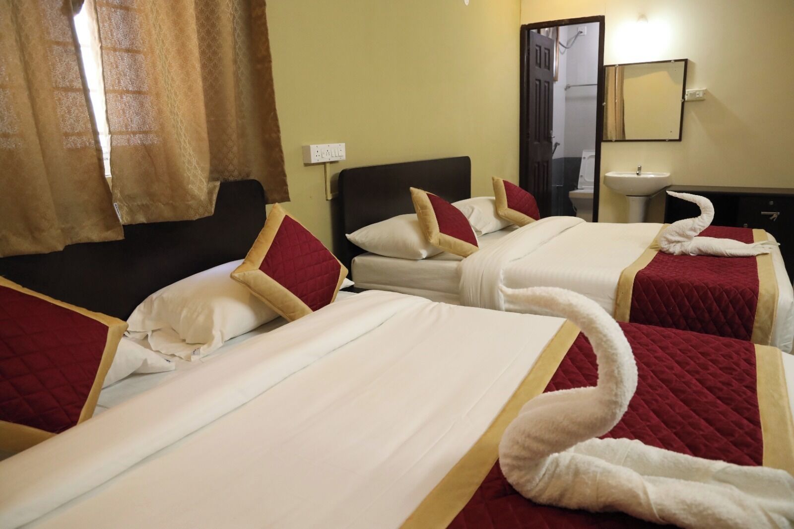 A hotel room with two beds, each with a red and white quilted bedspread, and a white towel on the beds.
