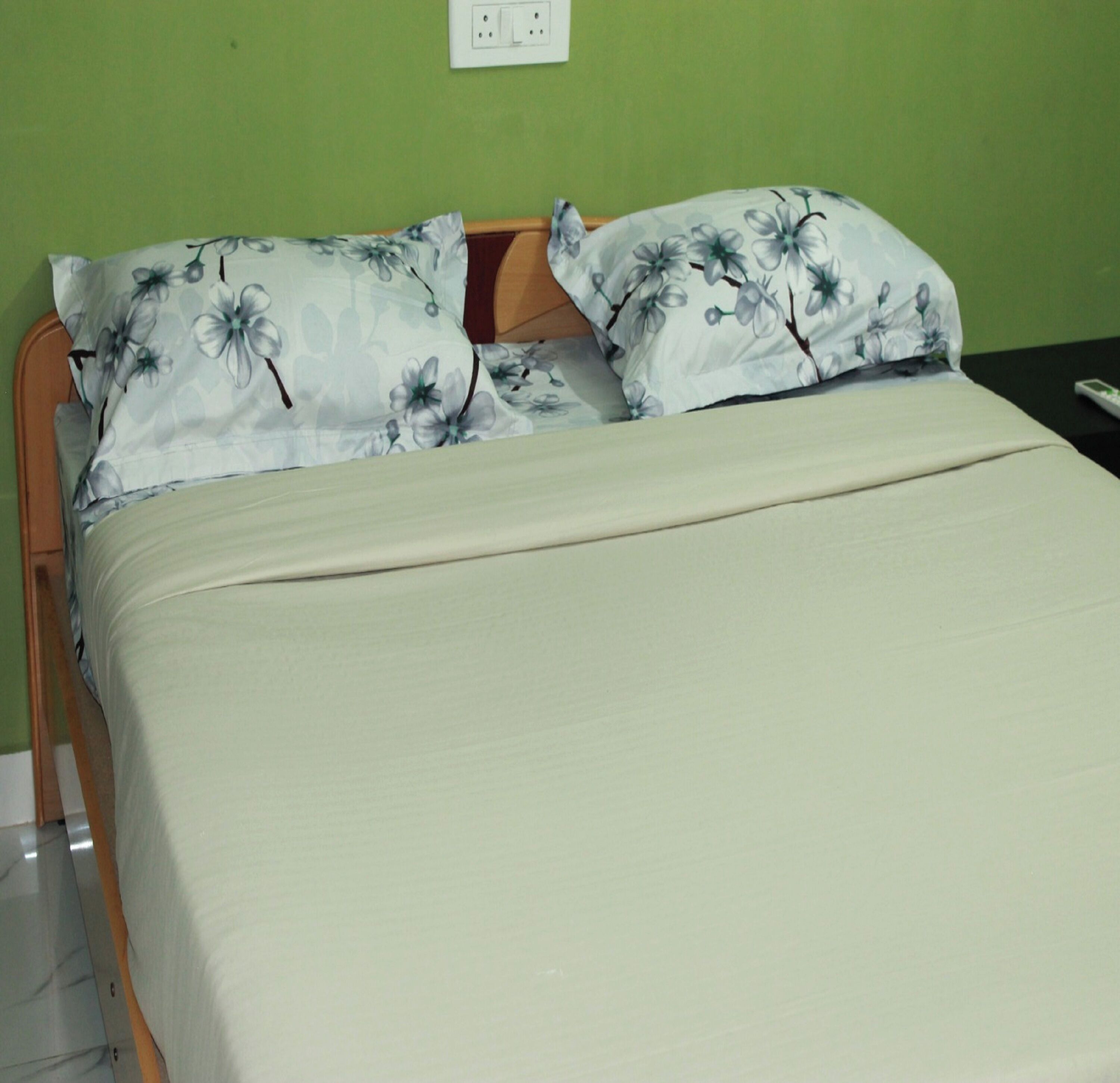 Una cama con almohadas estampadas con motivos florales y una colcha lisa en una habitación con paredes verdes y cabecera de madera.