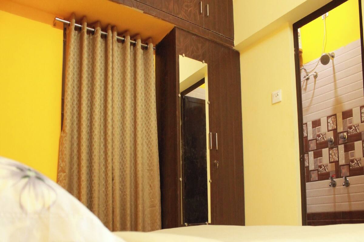 A hotel room with a bed, curtains, a wardrobe, and a bathroom visible through an open door.