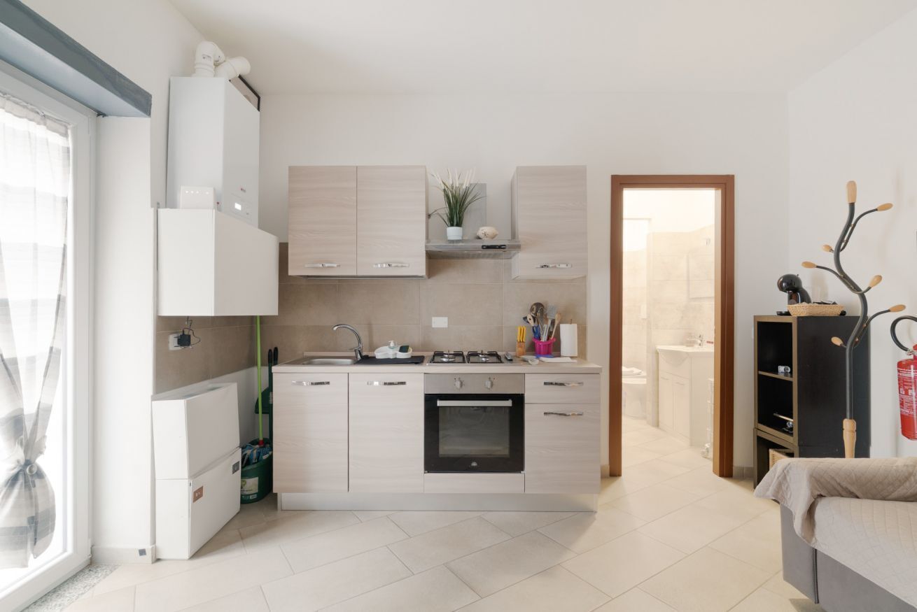 A modern kitchen with a built-in oven, a sink, and a stove. There is a small refrigerator to the left, and a wooden cabinet above the counter.