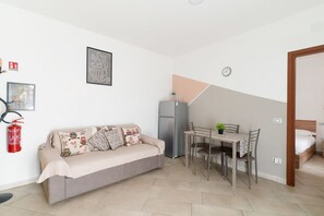 Een knus woongedeelte met een bank, een eettafel, stoelen, een koelkast, een klok en een bed.