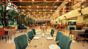 A spacious indoor dining area with multiple tables and chairs, featuring a high ceiling with exposed beams and string lights. - Yatri Niwas By Hotel Suraj Inn (Silvassa)