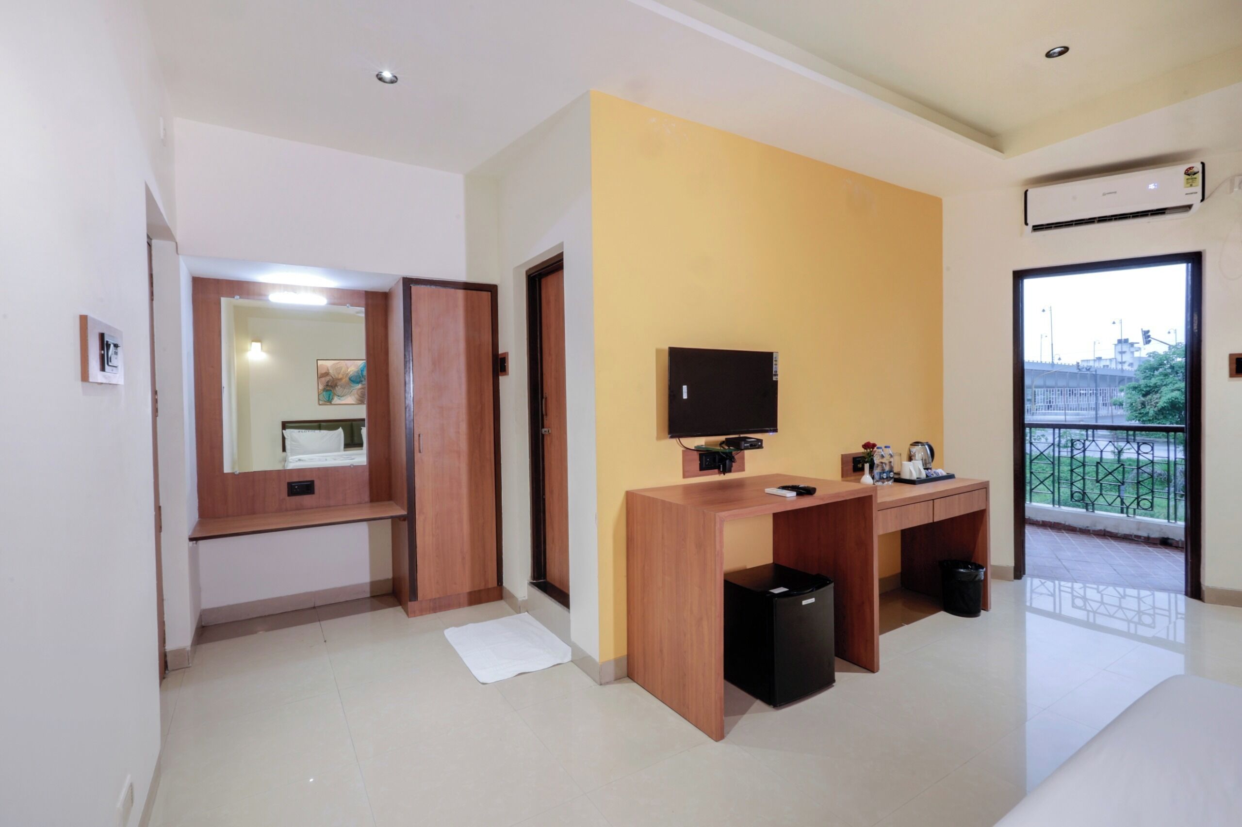 A hotel room with a wooden desk, a television, a small trash bin, and a window with a view of the outside.
