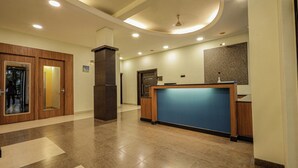 A modern hotel lobby with a reception desk, a wooden door, a blue counter, and a ceiling with recessed lighting. - Yatri Niwas By Hotel Suraj Inn (Silvassa)