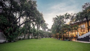 A spacious outdoor area with a well-maintained lawn, surrounded by tall trees and potted plants. - Yatri Niwas By Hotel Suraj Inn (Silvassa)