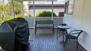 Uma área externa coberta com deck de madeira, churrasqueira, um banco e duas cadeiras.
