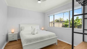 Quarto com cama, mesas de cabeceira e janela com vista para o verde.