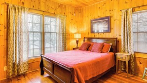 Un dormitorio con paneles de madera, una cama grande, dos mesitas de noche y una ventana con persianas.
