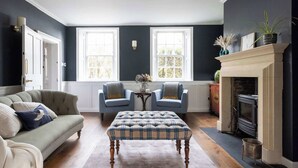 Een kamer met een donkerblauwe muur, een open haard, een bank, twee fauteuils en een tafel met een bloemenvaas.
