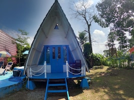Un edificio de forma triangular con puerta y ventanas azules, rodeado por una barrera de cuerda y una escalera que sube a la entrada.