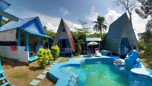 Un resort con varias cabañas de techo azul, una piscina y un pequeño puente.