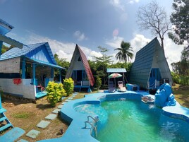 Un resort con varias cabañas de techo azul, una piscina y un pequeño puente.
