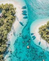 Vista aérea de una playa turquesa con varias embarcaciones amarradas a la orilla, rodeada de exuberante vegetación.