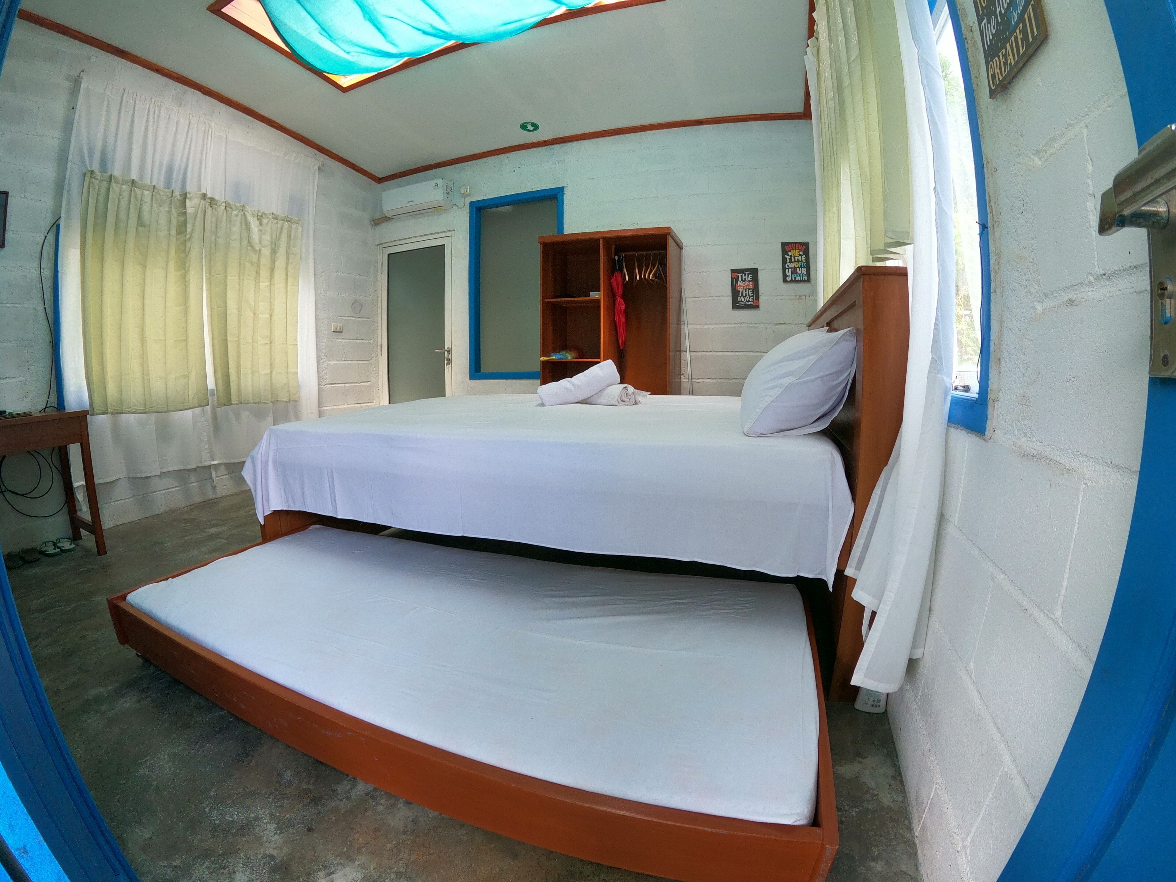 Una habitación con cama, armario, escritorio y ventana con cortinas.