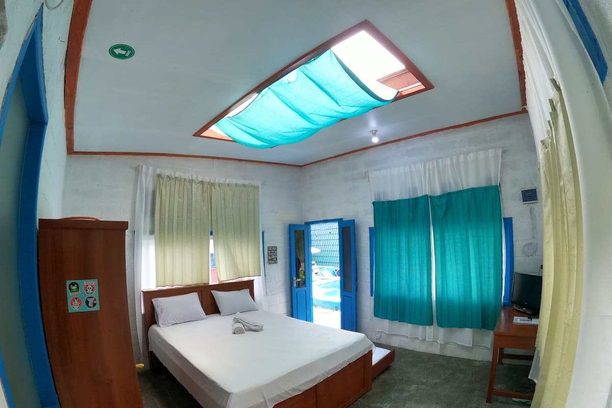 Ein Schlafzimmer mit einem Bett, einem Schreibtisch, einem Fenster mit Vorhängen, einer Tür und einer Deckenleuchte.