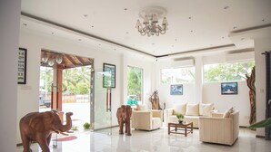 A spacious living area with a large elephant sculpture, a chandelier, and a sofa set.