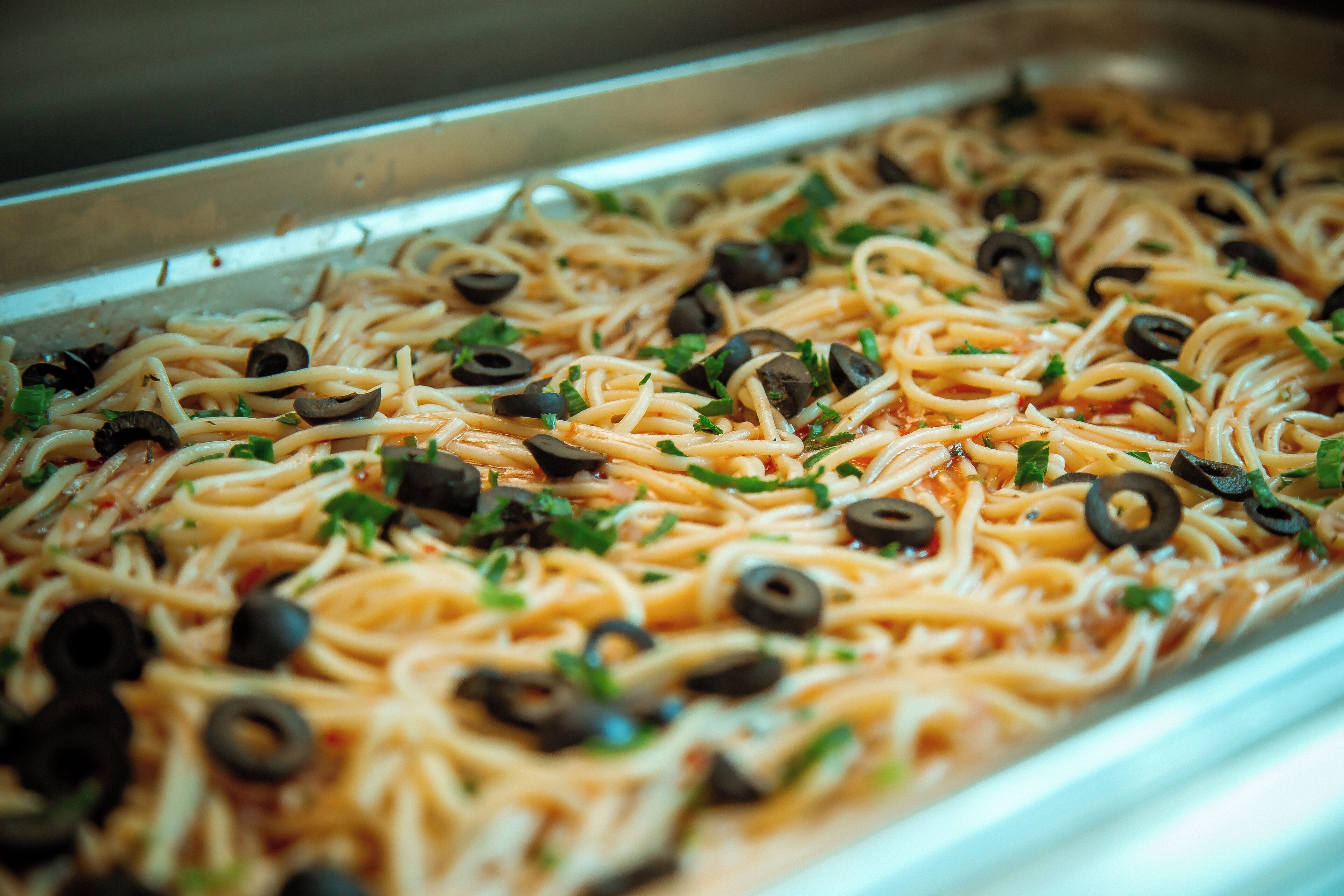 A tray of spaghetti with black olives and parsley.