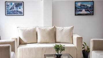 Una sala de estar con un sofá color crema, una mesa de centro de vidrio y dos plantas en macetas.