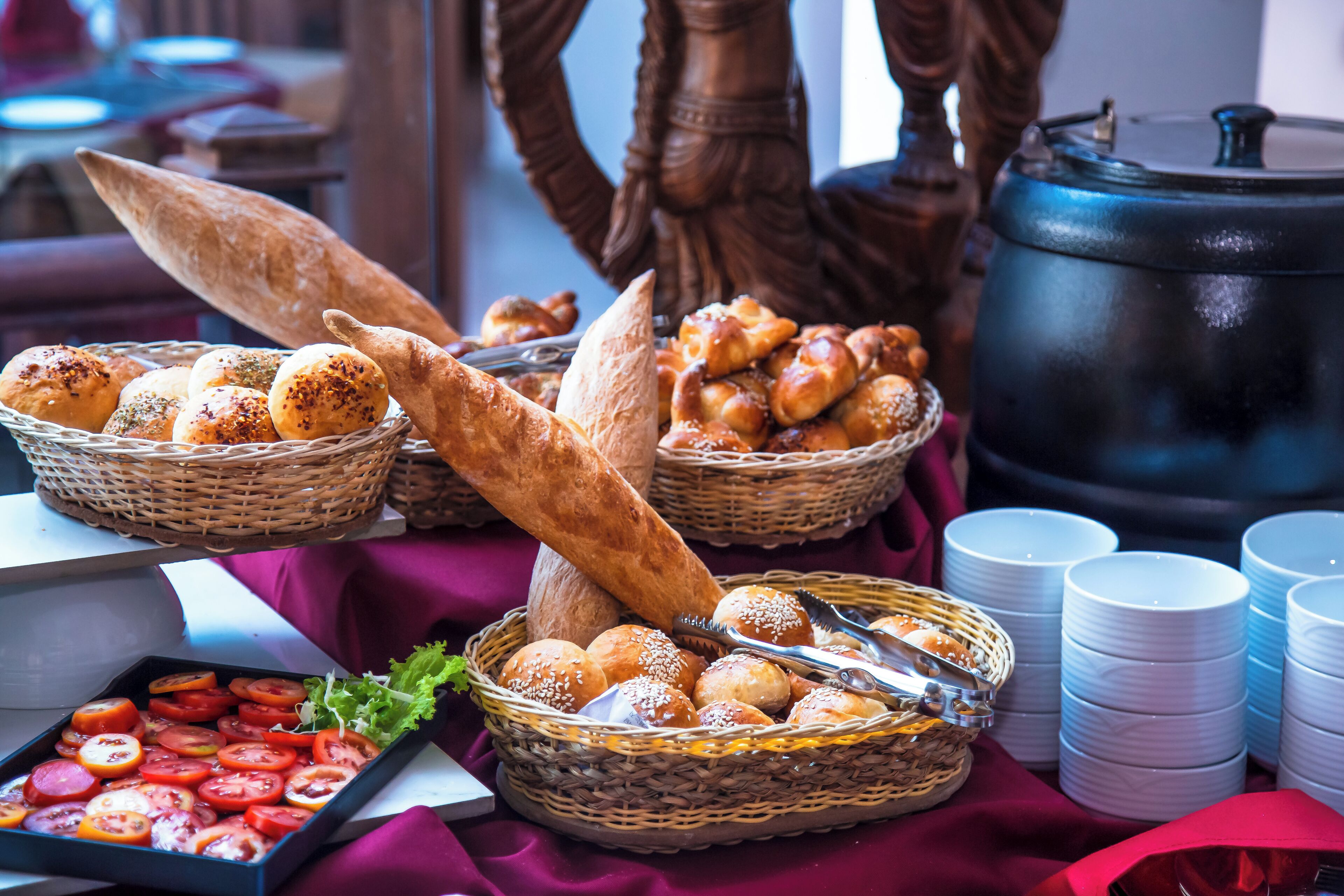 Une table de buffet avec divers pains, petits pains et un plateau de tomates coupées en tranches.