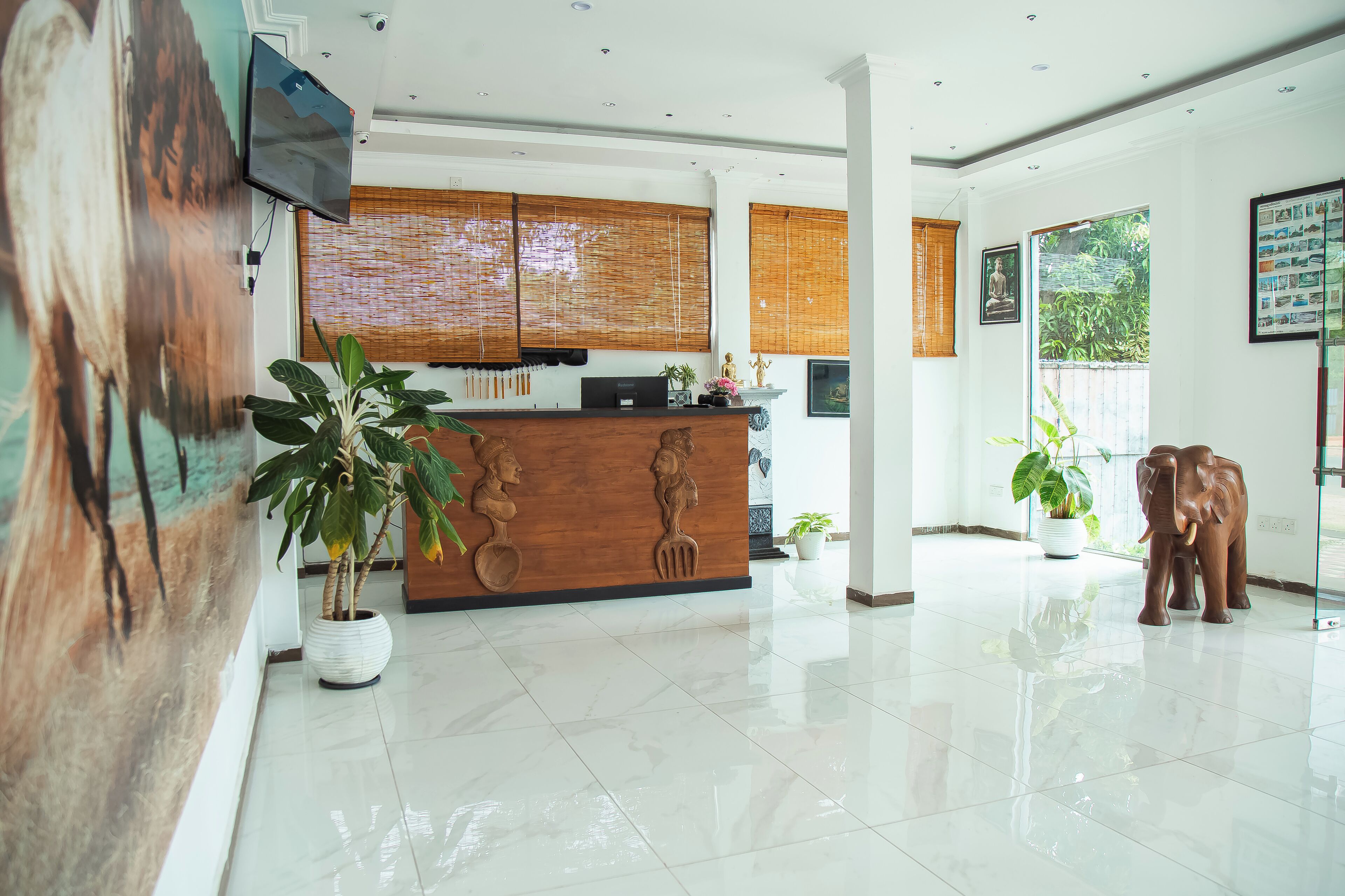 A reception area with a wooden counter, potted plants, a large painting, and a statue.