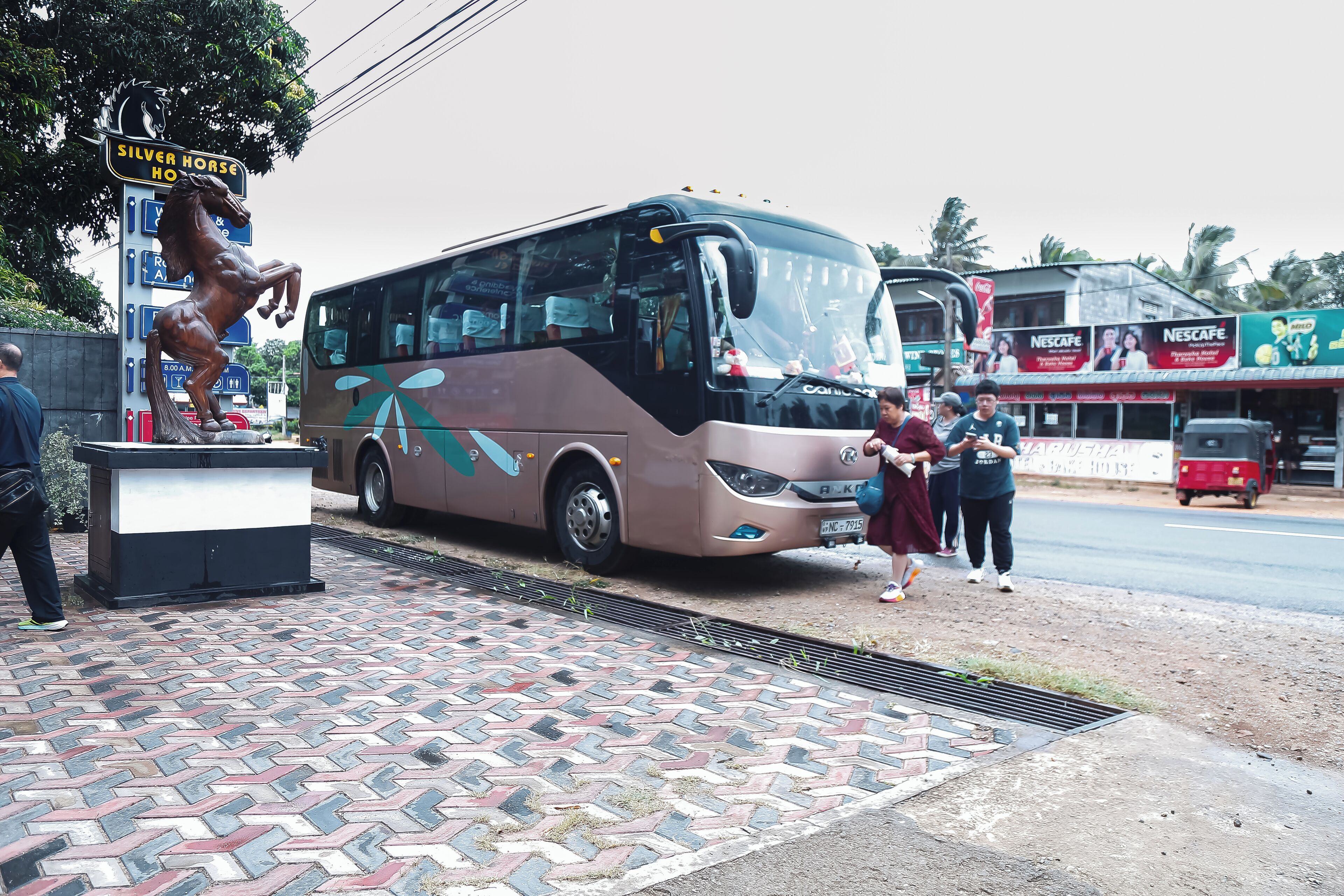 A bus parked at a bus stop with a statue of a horse and a sign that reads "Silver Horse Hotel".