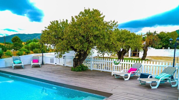 Una piscina con bordo in legno, recinzione in legno bianco e lettini da relax.