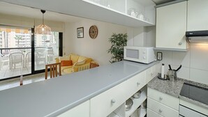 Cocina moderna con armarios blancos, microondas y comedor con sofá amarillo y sillas blancas.
