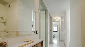 Un pasillo con suelo de mármol, un tocador de madera con espejo y una puerta que da a otra habitación.