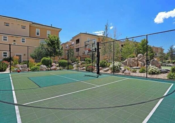 An outdoor tennis court with a net, surrounded by a fence, and residential buildings in the background. - South Reno 1BR · Pool, Events Center & Sauna (Reno)