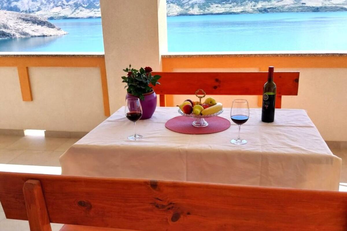 A table with a white tablecloth, two wine glasses, a bottle of wine, a fruit bowl, and a potted plant.
