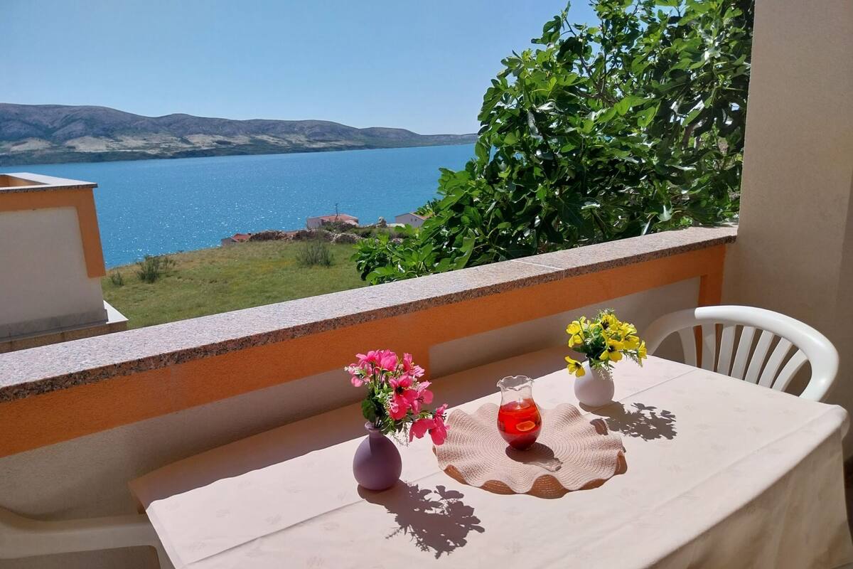 A balcony with a table set for two, overlooking a body of water and hills.