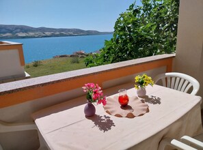 A balcony with a table set for two, overlooking a body of water and hills. - Metajna House With Pool And Sea View (Novalja)