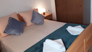 A neatly made bed with pillows, a bedside lamp, and a folded towel on a blue rug. - Metajna House With Pool And Sea View (Novalja)