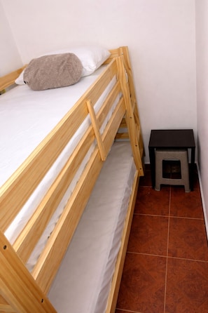 Een stapelbed met een kussen, een klein krukje en een betegelde vloer.