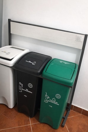 Drie vuilnisbakken met recycling symbolen, één zwart, één wit en één groen, geplaatst tegen een muur.