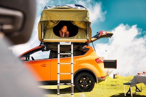 A camper with a tent roof, a ladder, and a table with bowls on a grassy field.