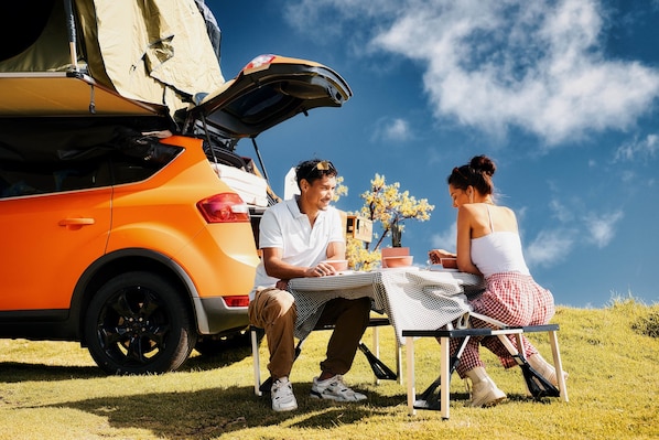 Two people sitting at a table with a car and tent in the background.