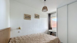 Une chambre à coucher avec un lit, une tête de lit en bois, une table de chevet, une lampe suspendue et deux tableaux encadrés accrochés au mur.