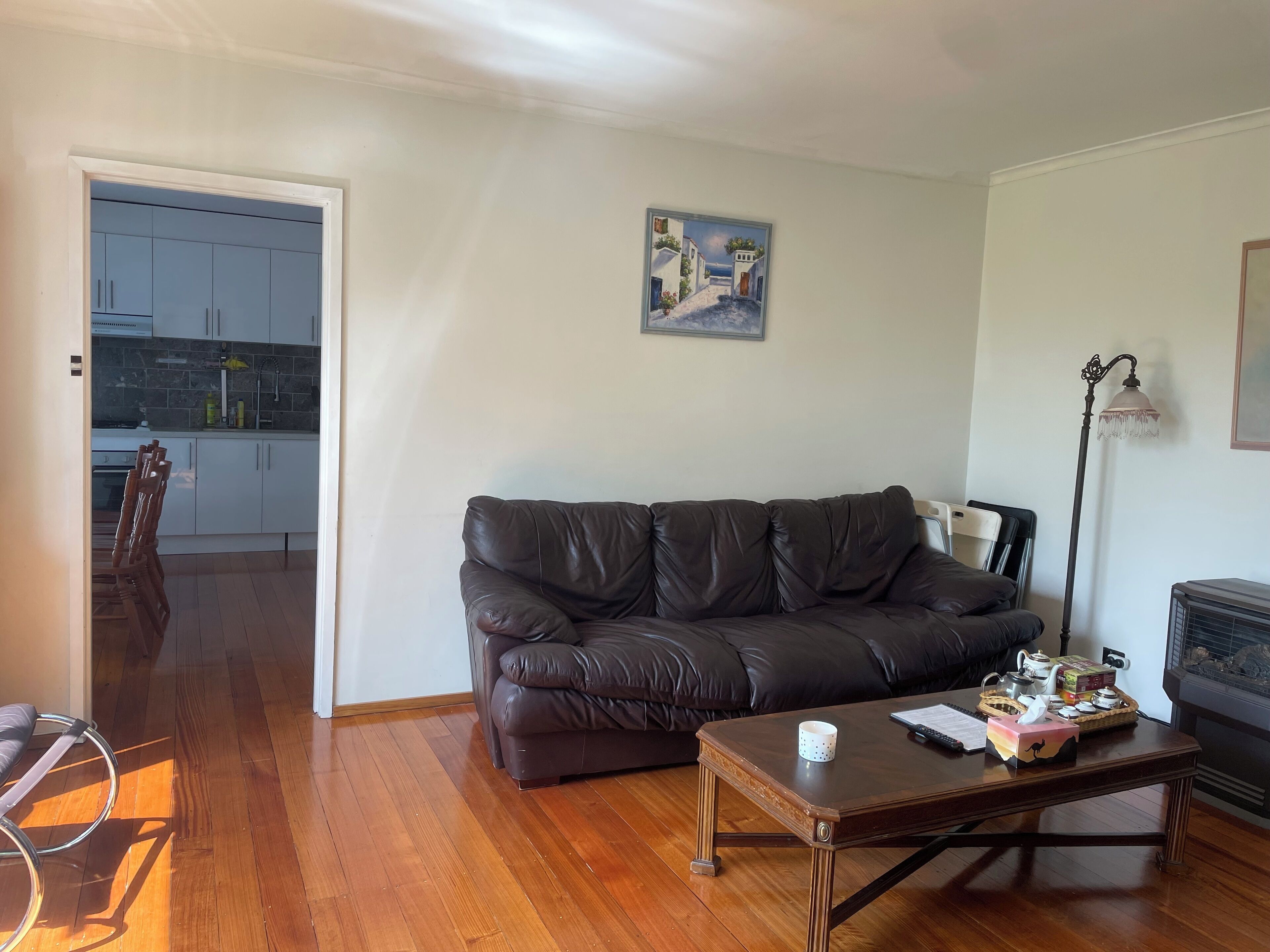 A living room with a dark leather sofa, a wooden coffee table, and a painting on the wall.