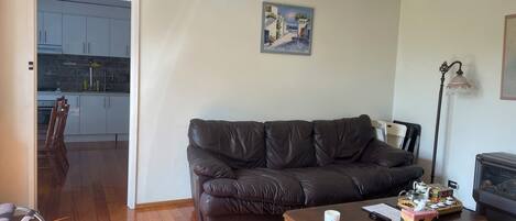 A living room with a dark leather sofa, a wooden coffee table, and a painting on the wall.