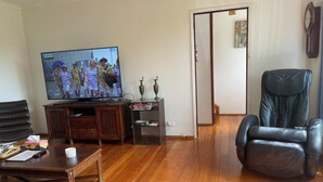 Una sala de estar con piso de madera, televisor, sillón de cuero, sofá, mesa de centro y aparador.