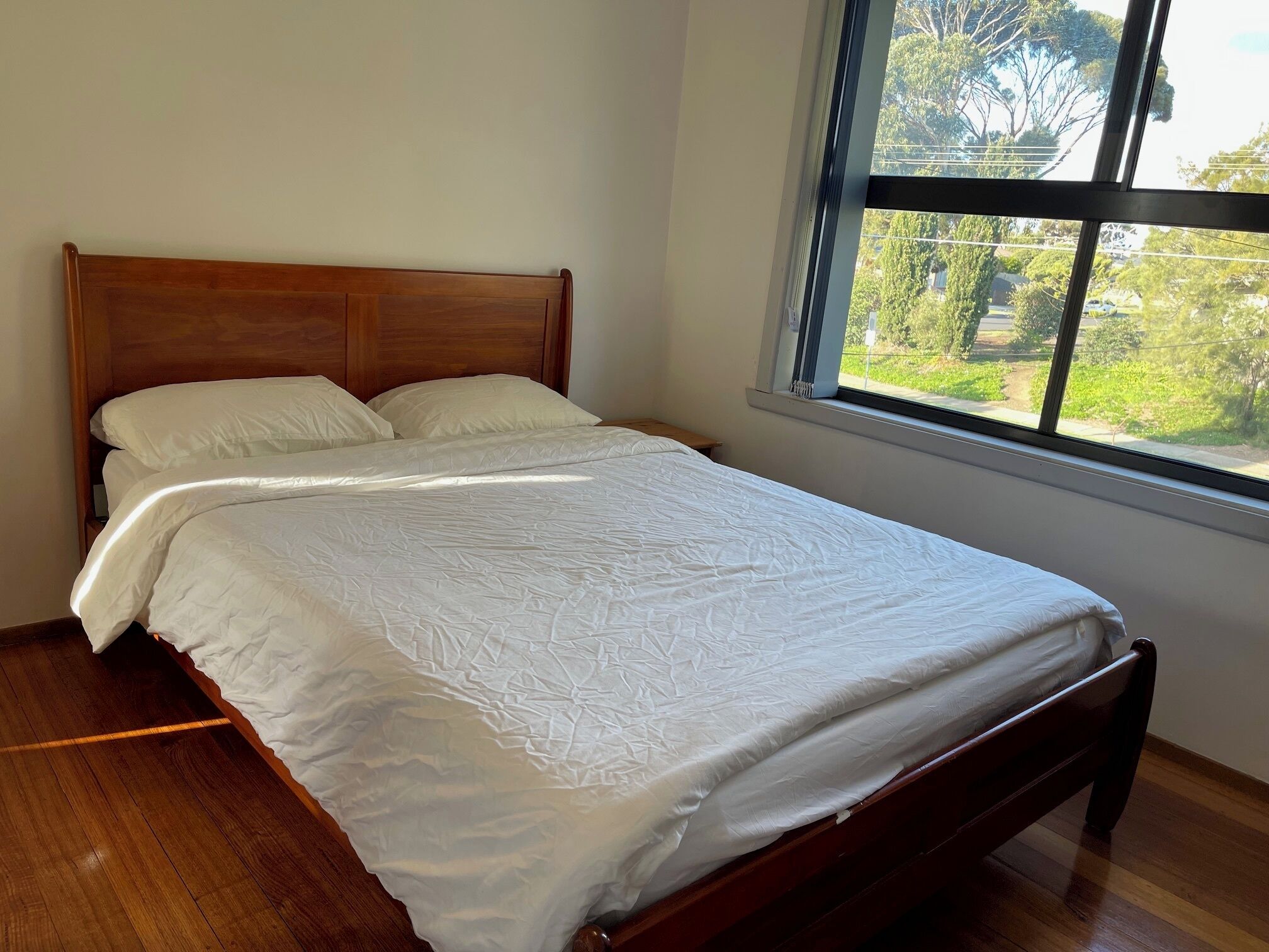 Un lit bien fait, avec du linge de lit blanc, dans une pièce au plancher en bois et dotée d’une grande fenêtre.