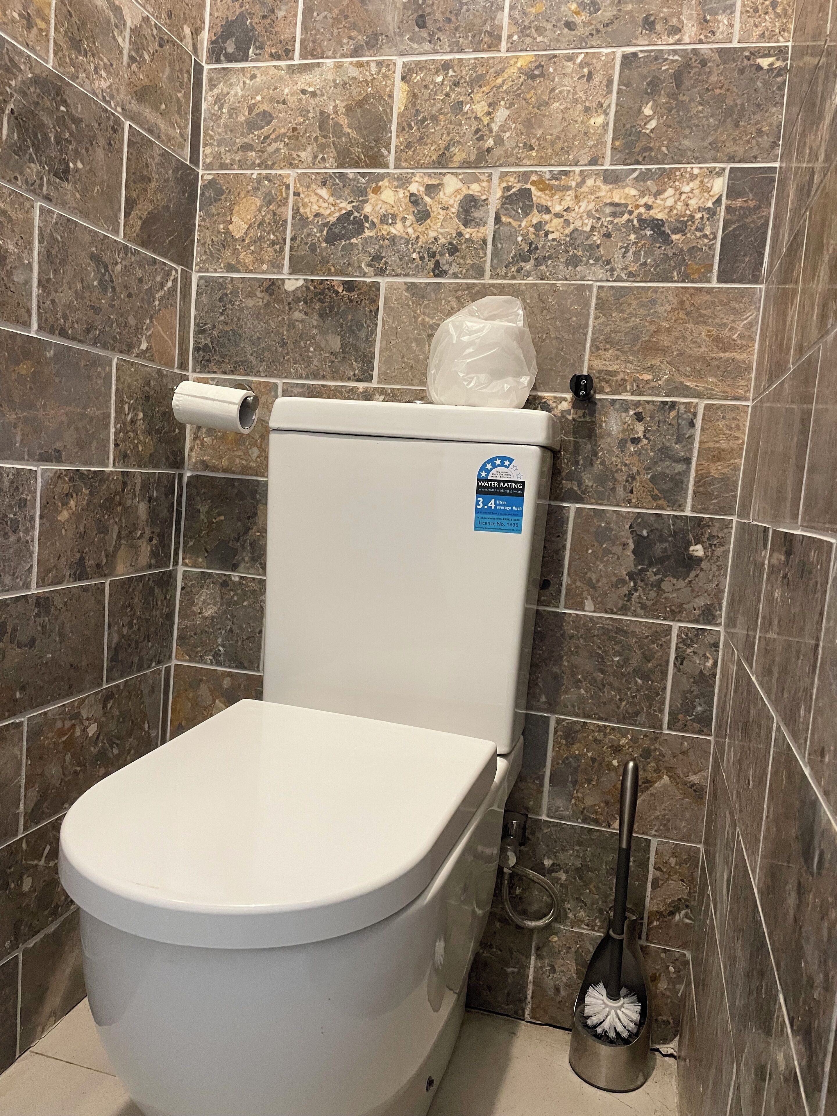 Et toilet med et vandforbrugsmærke, toiletpapirholder og en snave på gulvet.