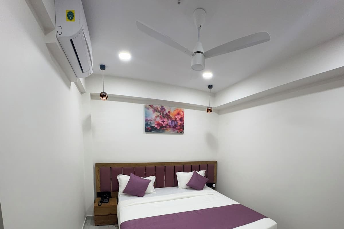 Un dormitorio ordenado con cama, ventilador de techo, equipo de aire acondicionado y un cuadro en la pared.