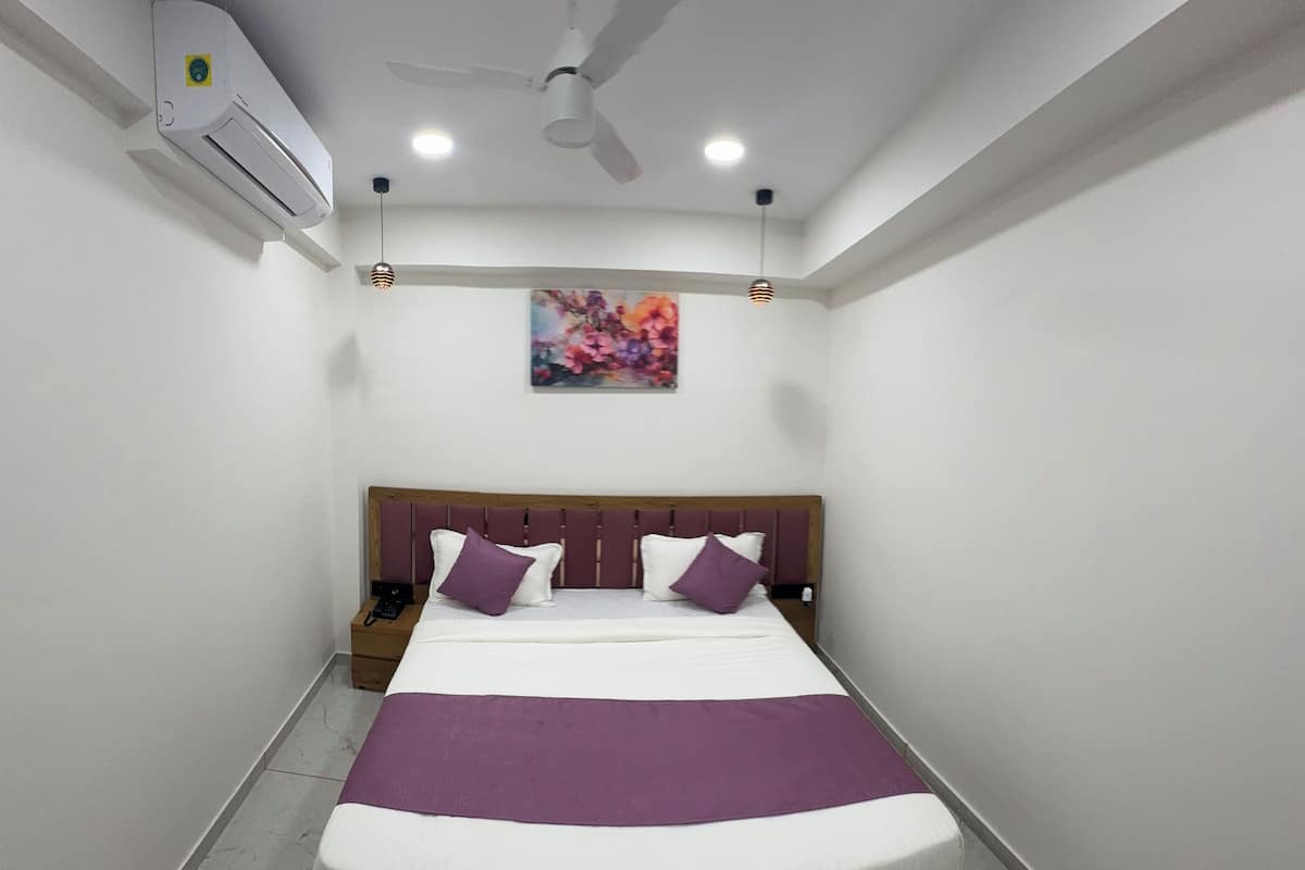 Un dormitorio ordenado con cama, ventilador de techo, unidad de aire acondicionado, mesita de noche y un cuadro colgado en la pared.