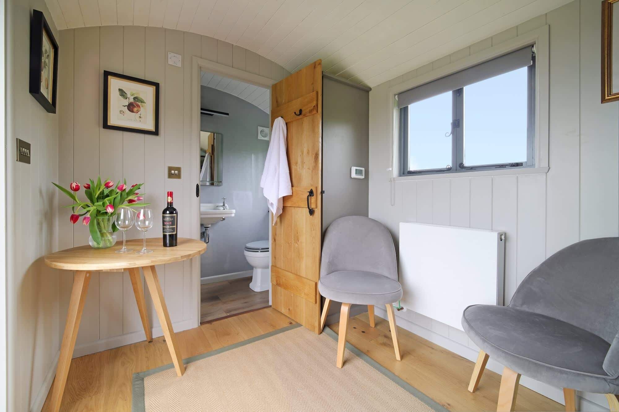 Une petite pièce avec une table en bois, deux chaises, un radiateur et une fenêtre.